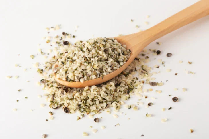 Hemp seeds spilling off of a wooden spoon with a white background