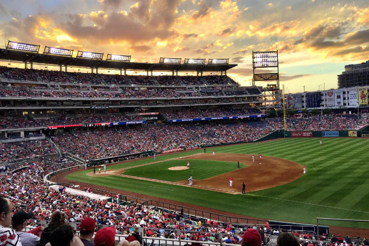 Baseball game in progress at a stadium with a colorful sunset sky